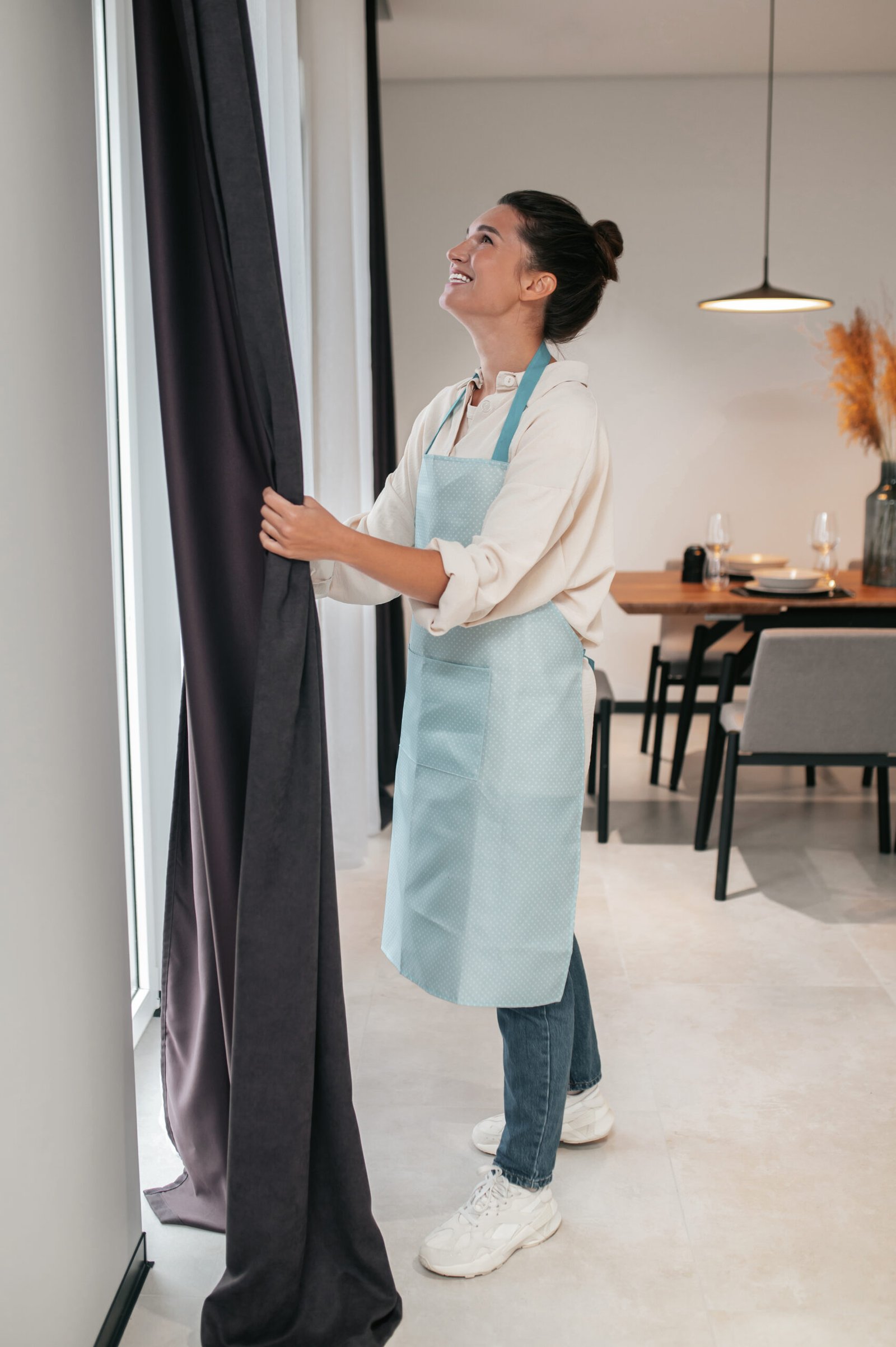 Daily routine. Young woman standing near the widnow and fixing the curtains